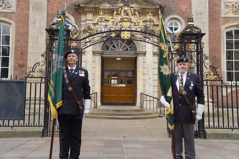 Two men in military uniform, bearing standards, stand outside the Worcester Guildhall gates
