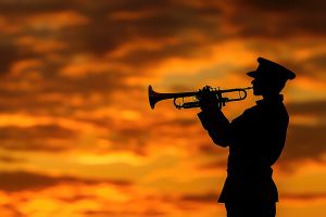 A soldier in uniform playing a trumpet, silhouetted against a sunset