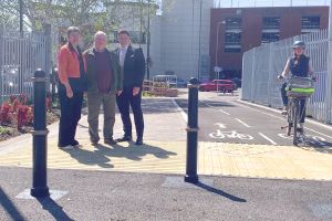 Three people standing at the entrance to a walking and cycling pathway, as another rides a bike along it