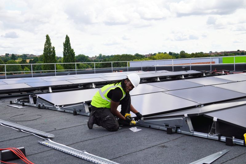 An engineer installing solar panels on the roof of the sports hall at Pediswell Leisure Centre, with Perdiswell Park visible in the distance.