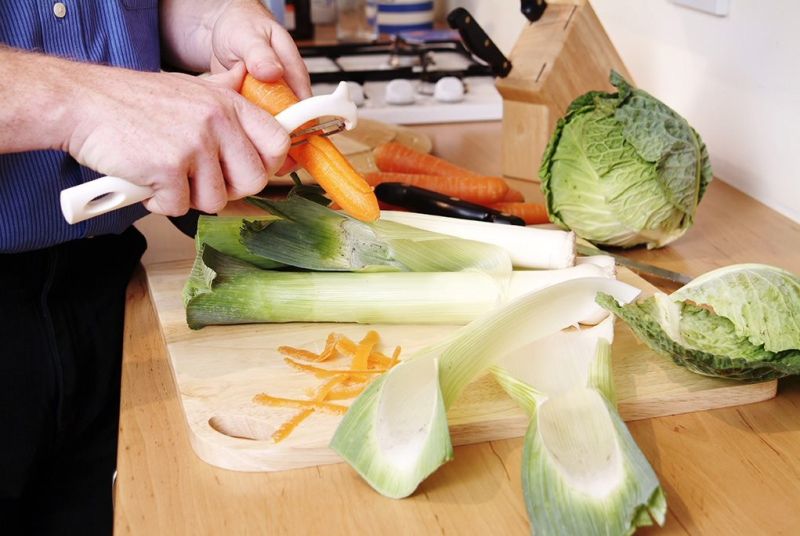 A cook is peeling and chopping carrots, leeks and cabbages