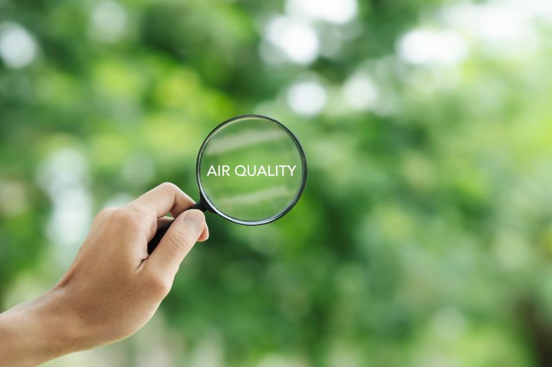 A hand holding up a magnifying glass, through which are visible trees and the words "air quality"