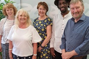 Five smiling people are standing in a brightly-lit room