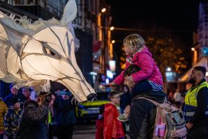 A little girl is holding her hand out to an illuminated puppet of a fox