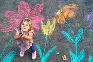A girl with chalk after chalking flowers on the floor
