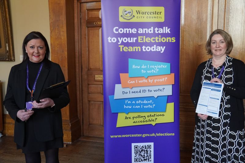 Two women standing to a banner that reads, "Come and talk to your Elections Team today"