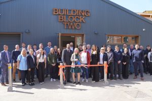 A crowd of peopled standing in front of a building on which is displayed a sign reading, "Building Block Two."