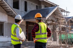 Two men in hard hats and high visibility jackets standing in front of a building that is under construction