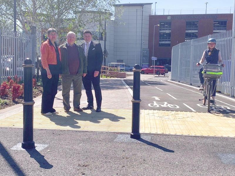 Three people standing at the entrance to a walking and cycling pathway, as another rides a bike along it