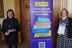 Two women standing to a banner that reads, "Come and talk to your Elections Team today"