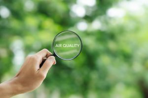 A hand holding up a magnifying glass, through which are visible trees and the words "air quality"