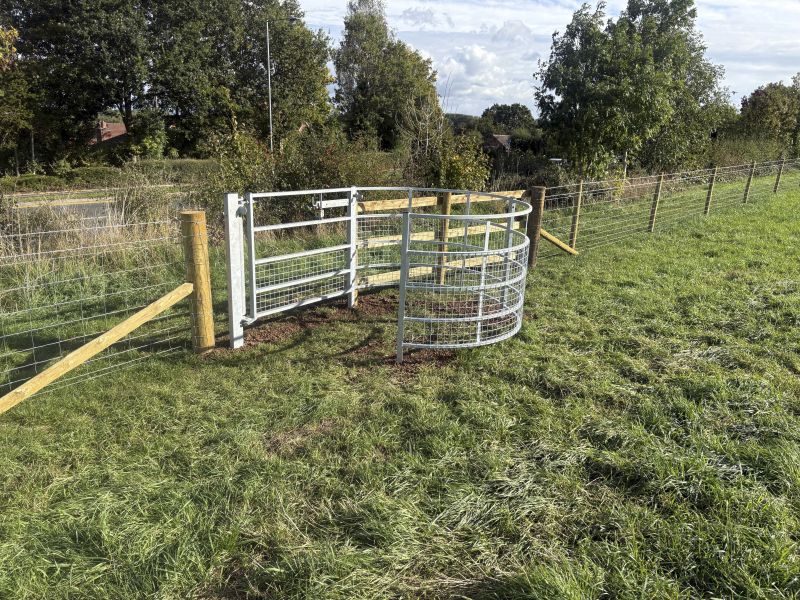 A metal kissing gate in a field, with trees behind