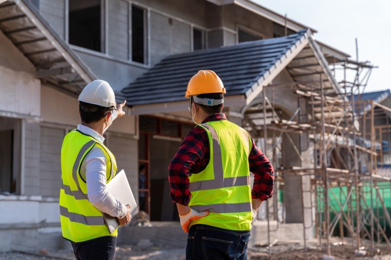Two men in high visibility jackets and hard hats looking at a half-built house